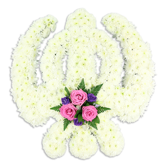 A beautifully composed Khanda floral tribute is presented against a crisp white background, its iconic Sikh symbolism rendered entirely in flowers with remarkable precision. The central double-edged sword rises upright, encircled by the perfect ring of the Chakra, while the outer Kirpans curve gracefully to either side, all of them shaped from densely packed white chrysanthemums or similar blossoms. Each bloom contributes a cluster of soft, overlapping petals, creating a plush, quilted texture that remains perfectly even across the whole design. From a short distance the surface appears like a serene blanket of white, yet up close you can almost trace the individual flowers that give it life. At the very bottom of the emblem, where the lower points of the crossed Kirpans nearly meet, a contrasting cluster of accent flowers draws the eye. Here, three pink roses open in balanced formation, their petals a gentle blush tone that suggests tenderness and remembrance. Around them, small deep purple flowers - perhaps lisianthus or freesia-style blooms - add quiet richness, while finely cut fern fronds and fresh green foliage create a soft frame that lifts the colours forward. Soft studio lighting falls evenly over the tribute, creating delicate shadows in the contours of the petals and a faint outline beneath, which makes the piece seem to hover slightly above the surface. This bespoke Khanda arrangement, often chosen for Sikh funerals and memorial tributes for families in Upton Park and neighbouring Green Street or East Ham, carries a strong sense of faith, honour, and continuity. It feels like a gentle yet steadfast statement of respect, crafted with the patient, steady hands of an experienced local florist.
